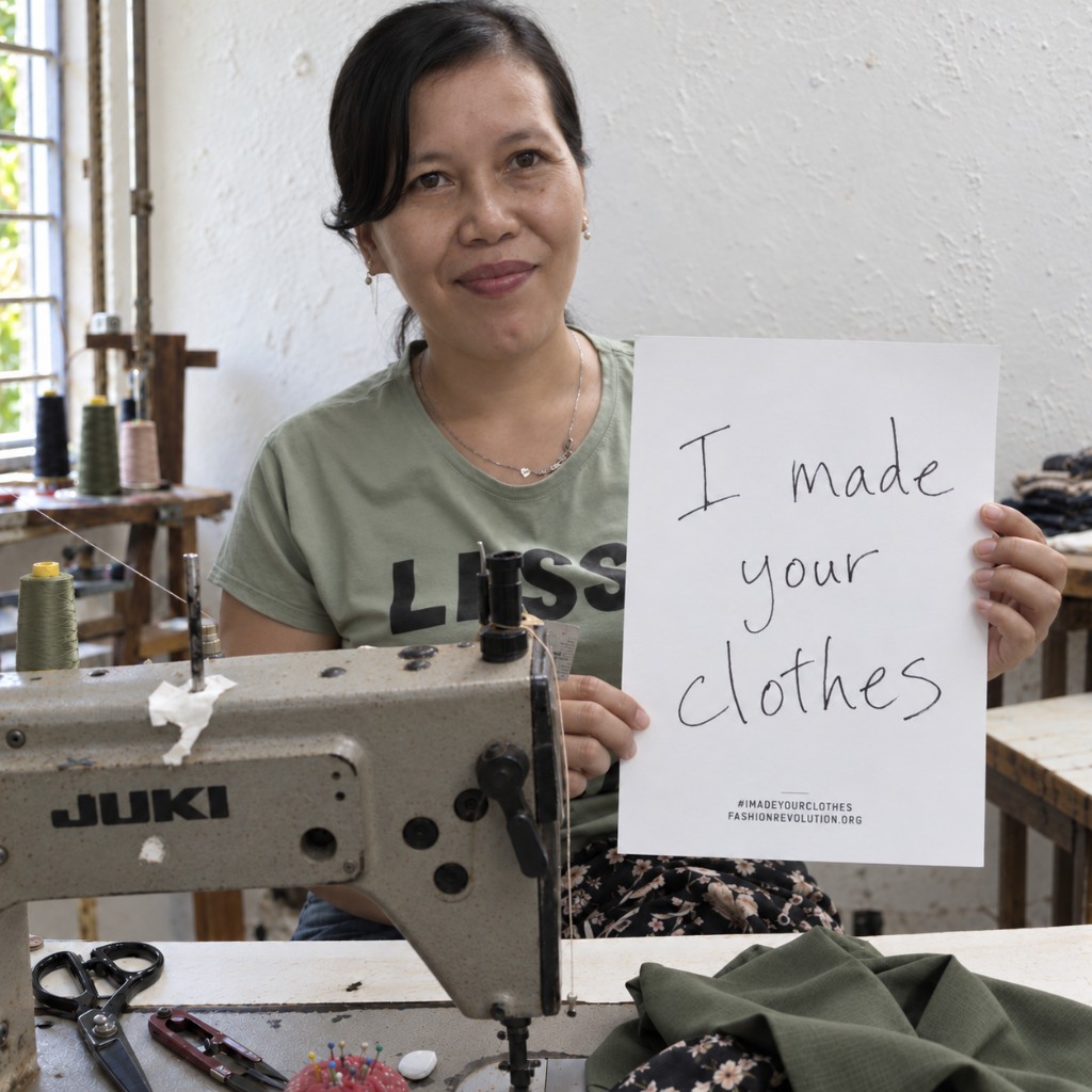 Artisan at a sewing machine holding an I made your clothes sign